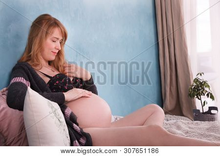 Expectant Mother Is Lying On The Bed, Smiling, Gently Stroking The Belly, Which Is Her Future Child