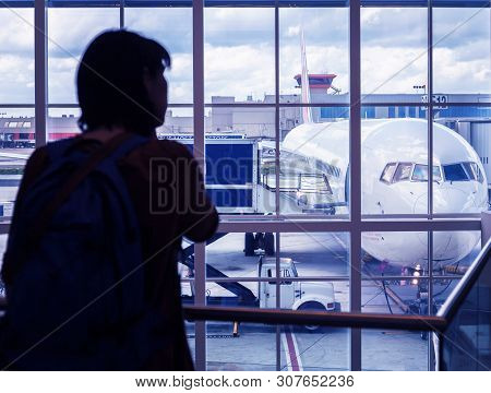 Silhouette A Young Woman Is Standing At The Airport By The Window Looking At The Pre-flight Preparat