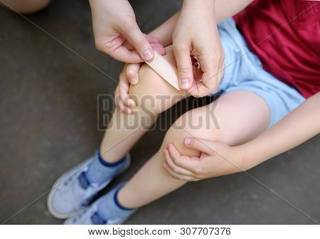 Mother Hands Applying Antibacterial Medical Adhesive Plaster On Child's Knee After Falling Down.