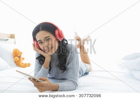 Close Up Shot Of Lovely Asian Woman Lie Prone, Prop Up, Smiles And Wearing Headphone That Connect To