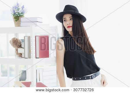 Sexy Asian Model Woman In Black Shirt And White Pants, Wearing Hat, Standing And Pompous, Studio Sho
