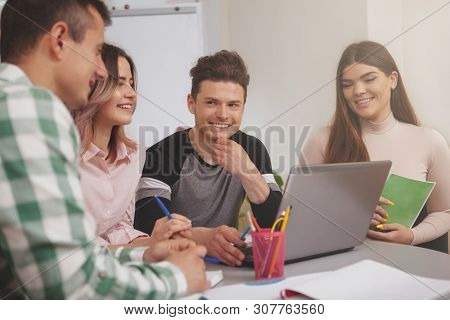 Cheerful Handsome Young Male Student Smiling Joyfully At His College Friends, While Studying Togethe