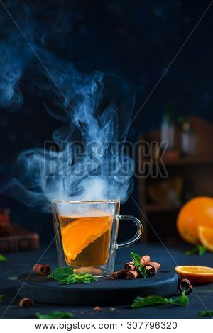 Double Wall Glass Cup With Citrus Tea, Cinnamon, And Mint Leaves. Steam In Dark Food Photography Wit