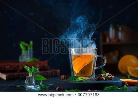Double Wall Glass Cup With Citrus Tea, Cinnamon, And Mint Leaves. Steam In Dark Food Photography Wit