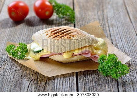Grilled And Pressed Panini With Ham, Melted Cheese, Cucumber And Tomato Served On Sandwich Paper On 