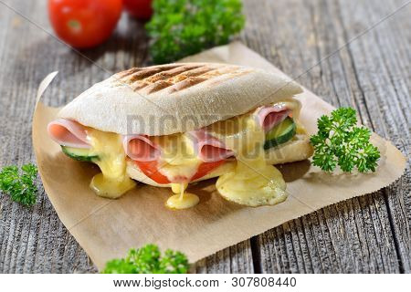 Grilled And Pressed Panini With Ham, Melted Cheese, Cucumber And Tomato Served On Sandwich Paper On 