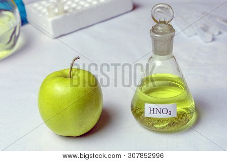 An Apple And A Chemical Flask Labeled Nitric Acid - Nitrate. The Concept Of The Presence Of Nitrates