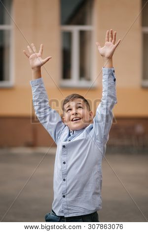 Happy Boy Jump And Raises Hands Up. Background Of School