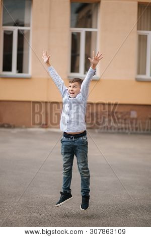 Happy Boy Jump And Raises Hands Up. Background Of School