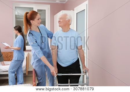 Nurse Assisting Senior Patient With Walker In Hospital Ward