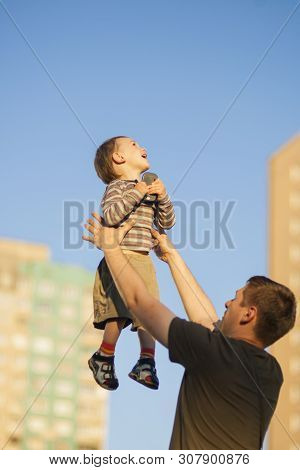 Father And Son Having Fun Together Outdoors.dad Tossing Son Up Against Blue Sky.  Vertcal Image