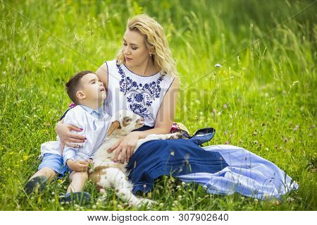 Mother Along With Her Little Son And Cub Of Newborn Lamb Posing Outdoors On Nature Background. Horiz