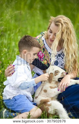 Smiling Mother With Her Little Happy Son And Cub Of Newborn Lamb Posing Outdoors On Nature Backgroun