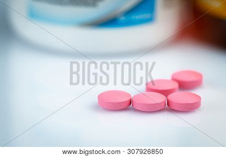 Round Pink Tablets Pill On Blurred Drug Bottle. Vitamins And Minerals Plus Folic Acid Vitamin E And 