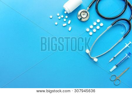 Pills And Medical Equiupments Including Stethoscope, Syringe And Scissors At Border On Light Blue Ba