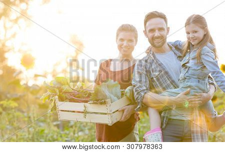 Portrait of smiling family with vegetables in crate at farm