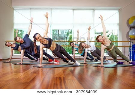 A Group Of Sporting Young People In Sportswear, In A Fitness Room, Doing Push-ups Or Planks In The G