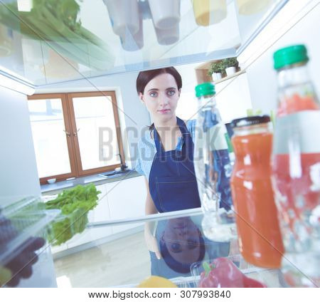 Portrait of female standing near open fridge full of healthy food, vegetables and fruits. Portrait of female