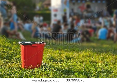 Red Litter On Green Grass. Garbage In The Nature After The Concert.