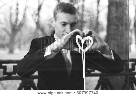 Sad Young Man In Love. The Guy Is Saddened Is Looking At The Painted Heart On The Window. Concept Br