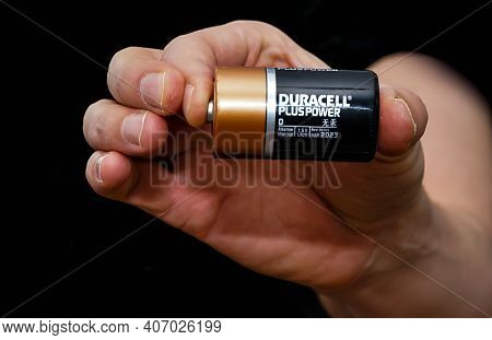 Close Up Of A Hand Holding A Duracell Battery, Isolated On A Black Background. Shallow Depth Of Fiel