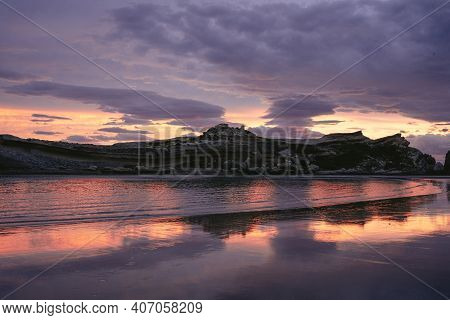 Amazing Sunset At The Beach With Cliffs Reflected On The Water. Castle Point, New Zealand.