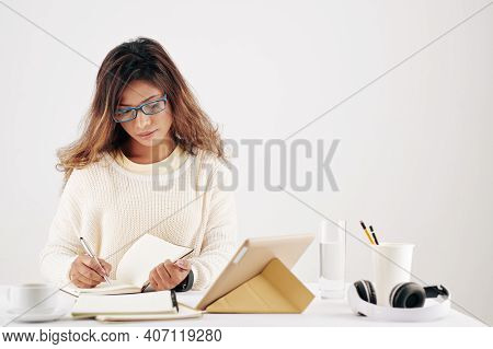 Serious Young Aisan Businesswoman In Glasses Working At Office Desk And Writing Down Pans And Creati