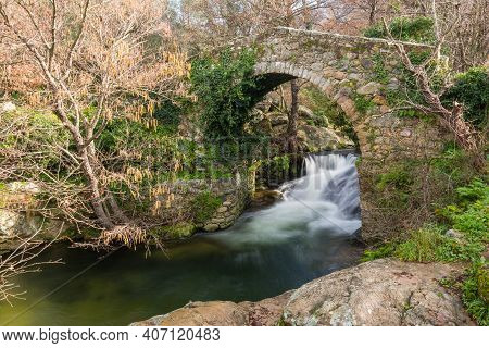 Mountain Stream Rushing Through A Woodland And Cascading Beneath An Ancient Genoese Bridge Near Feli