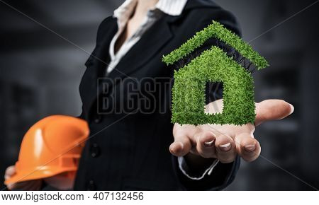 Real Estate Agent Holds In Palm Green Plant In Shape Of House. Woman In Business Suit With Safety He