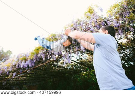 6-year Old Is Flying In His Dads Arms Under A Wysteria Tree