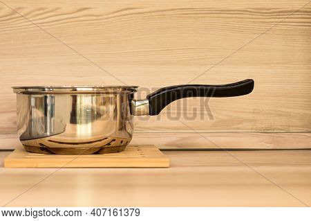 Stewpan On Wooden Table Top. A Metal Stewpan Made Of Stainless Steel Against Background Of Beige Woo