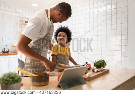 Happy Black Family. African American Father And Little Son Doing Online Cooking With Digital Tablet 