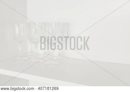 Dishes In Kitchen. Transparent Glass Wine Glasses, Stand On White Shelf In Kitchen Cabinet. Selectiv