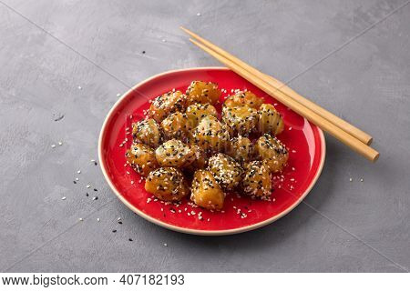 Traditional сhinese Fried Apples In Caramel With Sesame Seeds On Red Vintage Plate With Chopsticks O