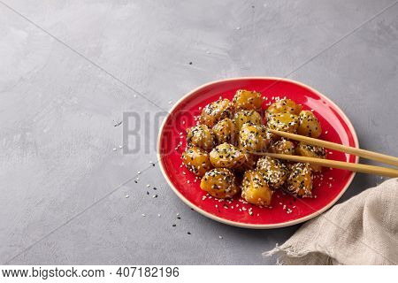 Traditional сhinese Fried Apples In Caramel With Sesame Seeds On Red Vintage Plate With Chopsticks O