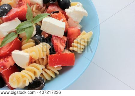 Itlian Fusilli Pasta Salad With Olives, Tomato, And  Feta Cheese In Blue Bowl On White Table Backgro