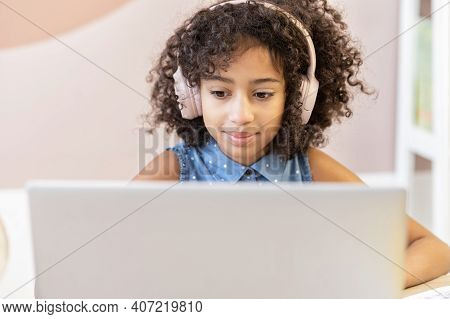 A Pretty Curly African Schoolgirl Wearing A Headphones Using A Laptop For Studying On The Distance, 
