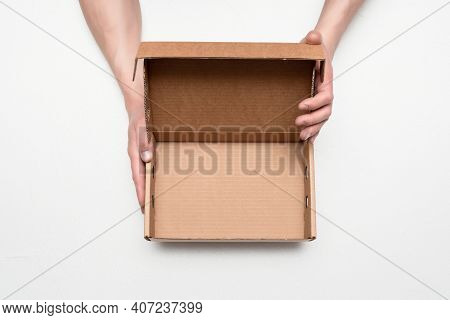 Empty Cardboard Box With Copy Space In The Male Hands On The Gray Background.