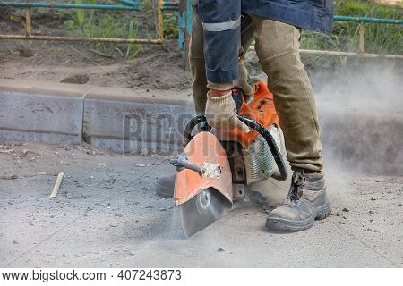 A Worker Uses A Portable Petrol Saw And A Diamond Cutting Blade To Cut Old Asphalt In A Cloud Of Dus