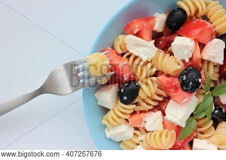Itlian Fusilli Pasta Salad With Olives, Tomato, And  Feta Cheese In Blue Bowl On White Table Backgro