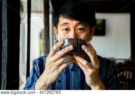 Young Adult Chinese Man In Traditional Costume Drinking A Cup Of Hot Tea In Chinese Restaurant. Mind