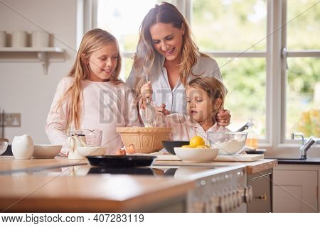 Mother And Two Daughters Making Pancakes In Kitchen At Home Together