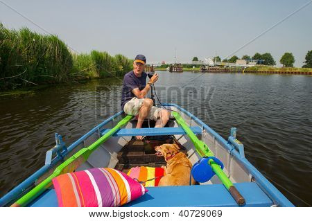Homem sênior com dog em pouco rowingboat no Rio holandês