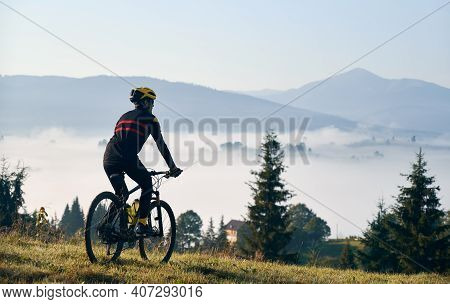 Silhouette Of Man Cyclist In Cycling Suit Riding Bike On Grassy Hill. Male Bicyclist Enjoying The Vi