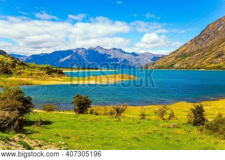 Green grassy mountains surround the magnificent Hawea Lake. South Island, New Zealand. Journey to the ends of the world. The concept of ecological, active and photo tourism