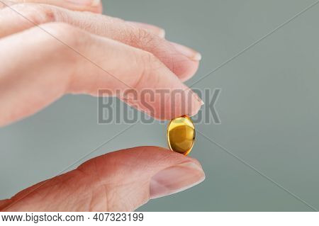 Female Hand Holding A Small Yellow Capsule Of Nutritional Supplement. Food Supplement, Vitamin D, Om