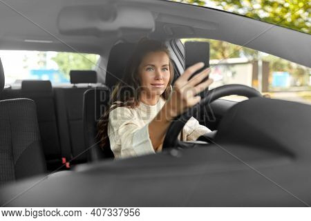 safety and people concept - happy smiling young woman or female driver driving car and taking selfie with smartphone