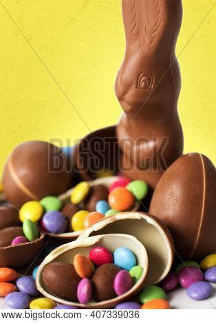 easter, sweets and confectionery concept - close up of chocolate bunny, eggs and candy drops over yellow background
