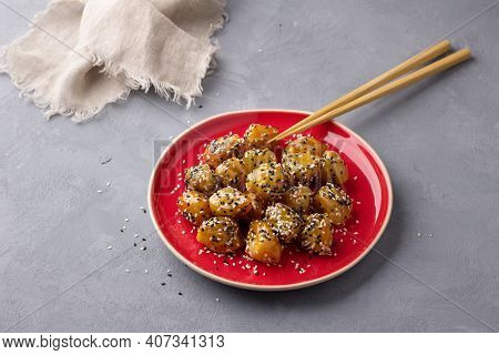 Traditional сhinese Fried Apples In Caramel With Sesame Seeds On Red Vintage Plate With Chopsticks O