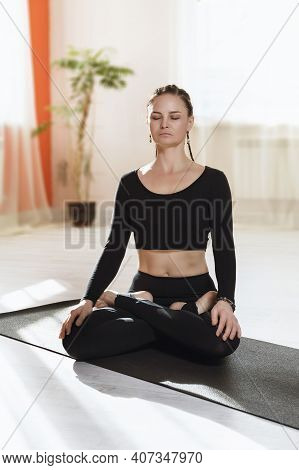 A Woman In Black Sportswear Practicing Yoga Sitting On A Gymnastic Mat In A Lotus Position Is Engage